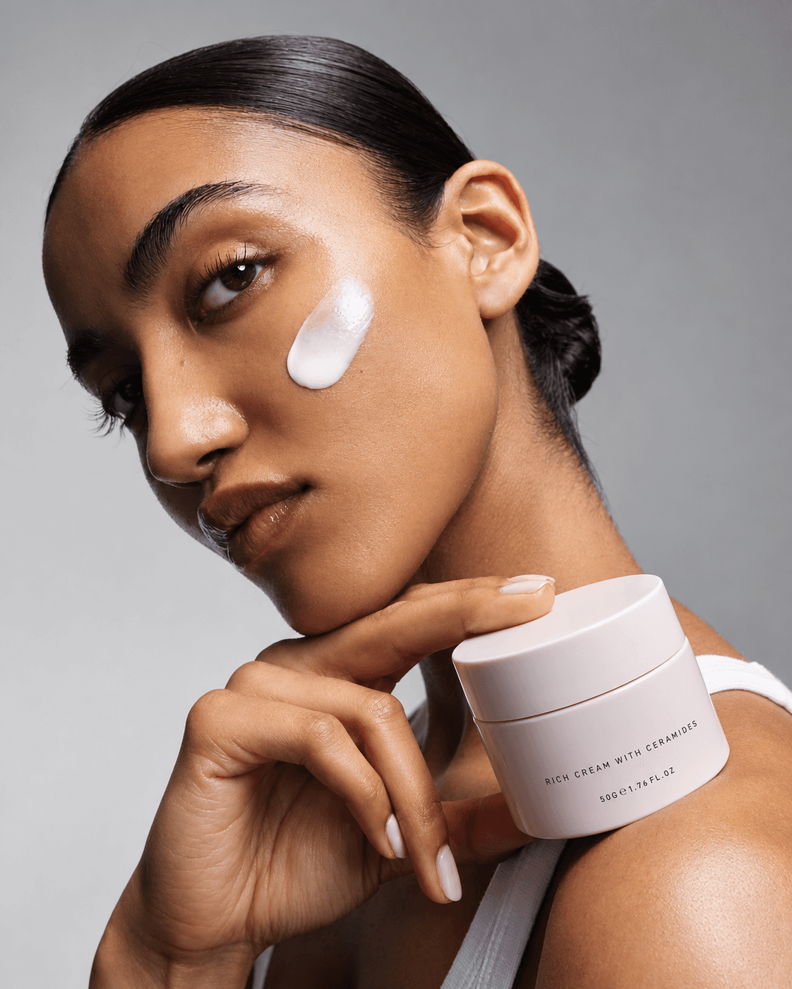 A woman holding a jar of rich cream in front of her face, the label turned to camera.
