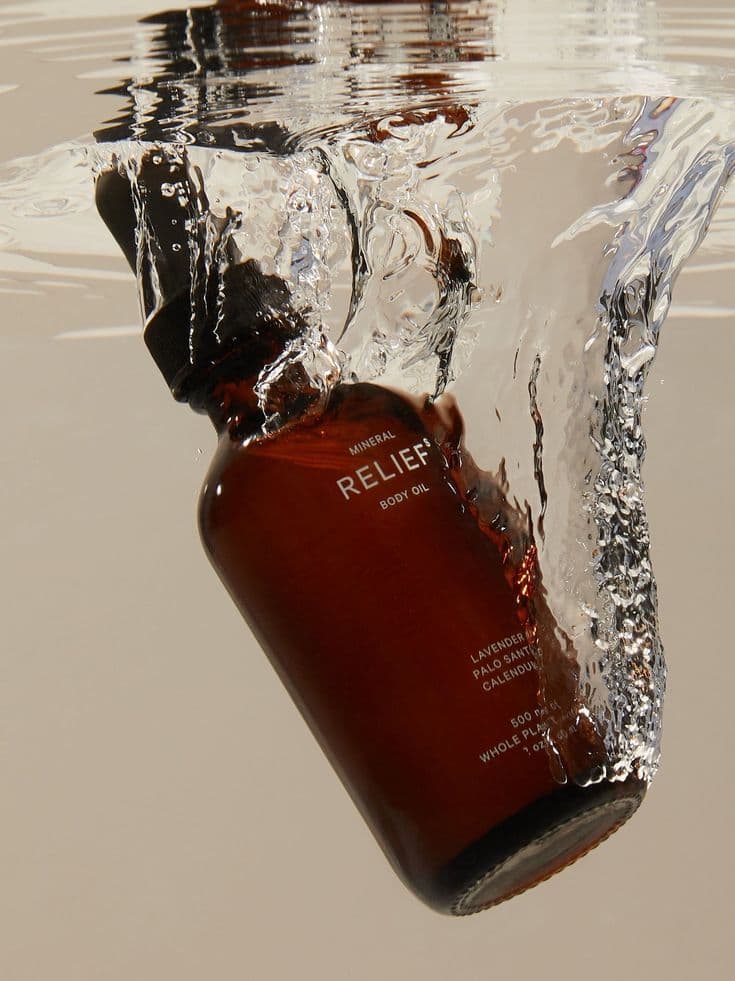 An amber glass bottle breaching the surface of water, mid splash.