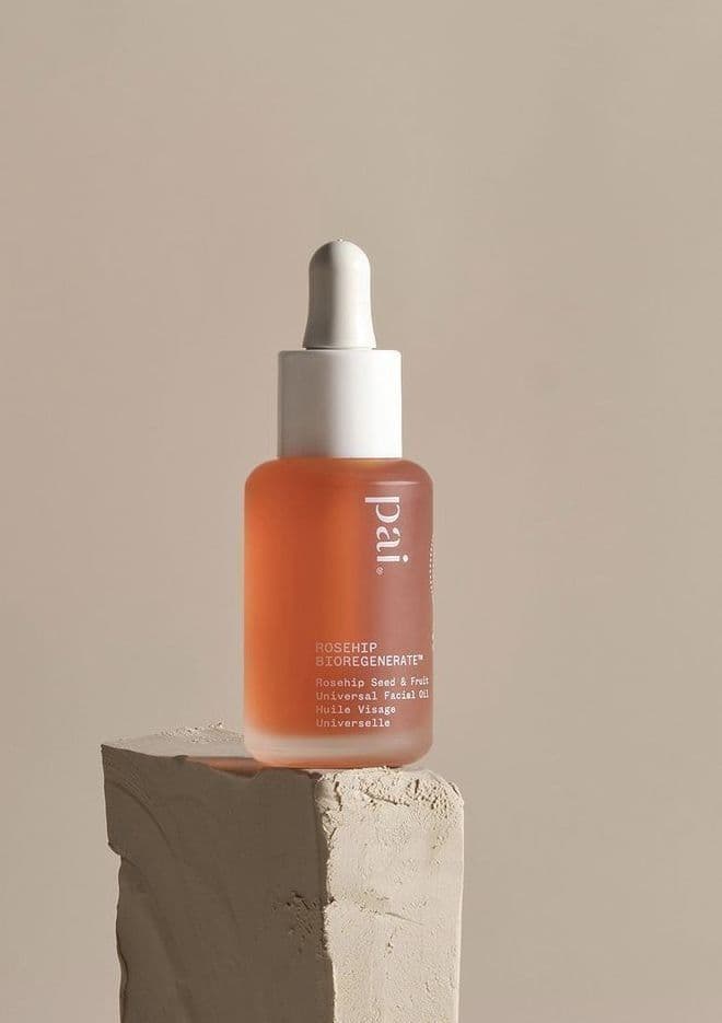 A blush coloured oil in a glass dropper bottle resting on a rough plaster block.